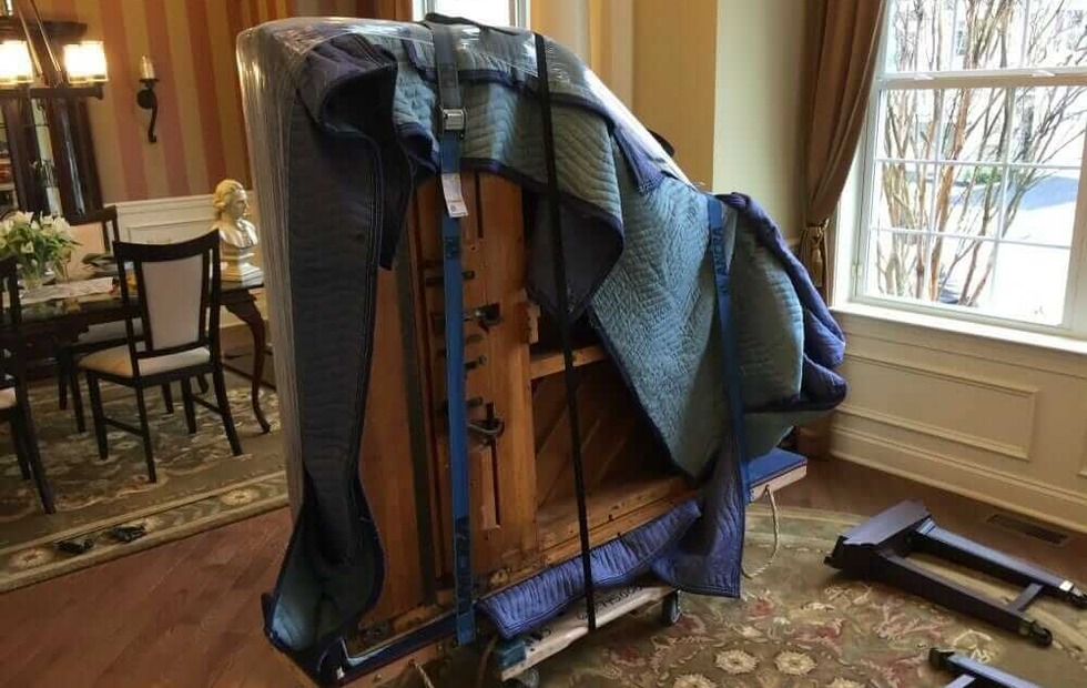 Piano movers wrapping an upright piano for transport